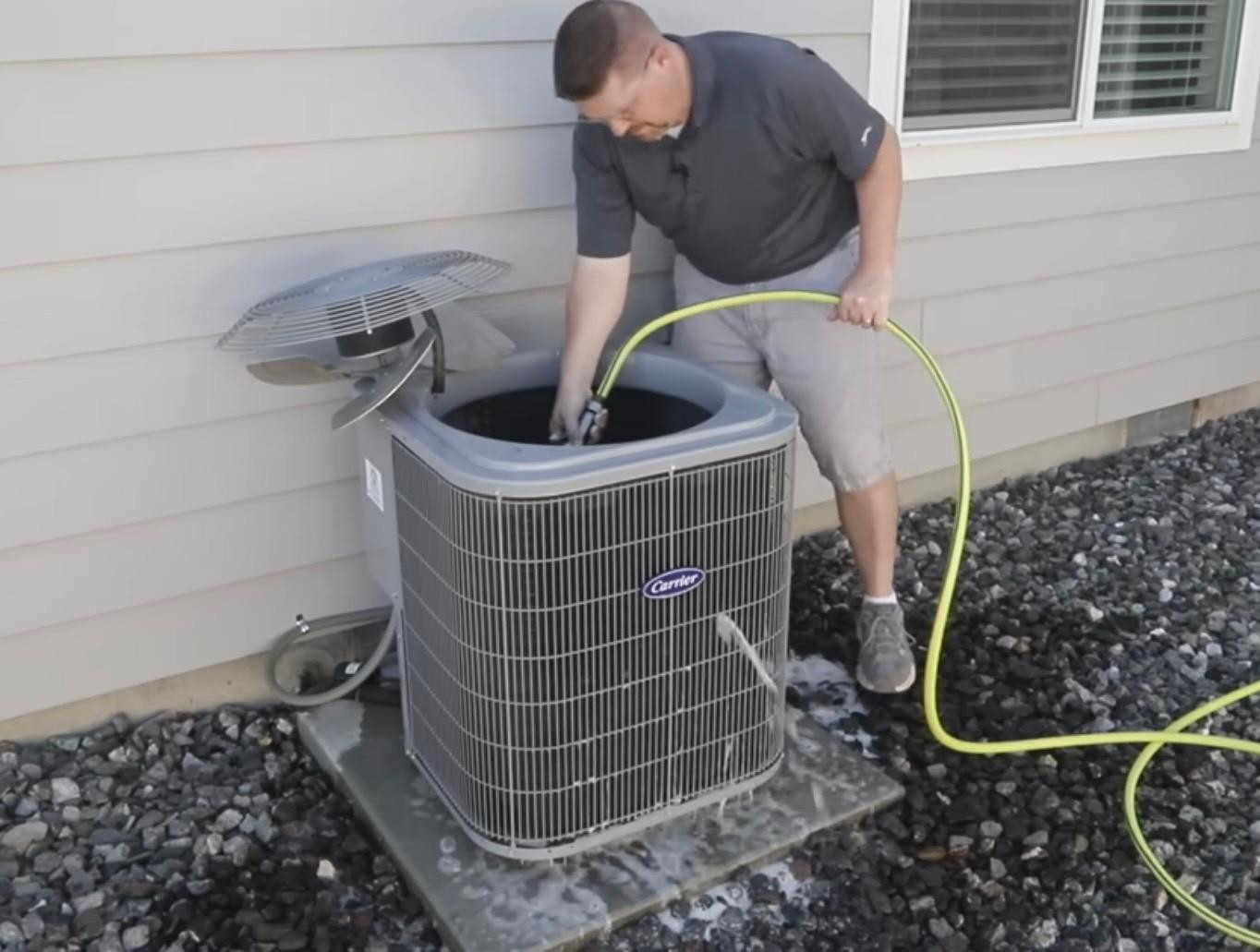 A GPS Heating and Air technician servicing an outdoor Carrier air conditioning unit at a customer's home
